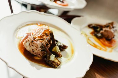 Lüks bir restoranda garsonların servis ettiği enginar ve sulu soslu domuz filetosu..