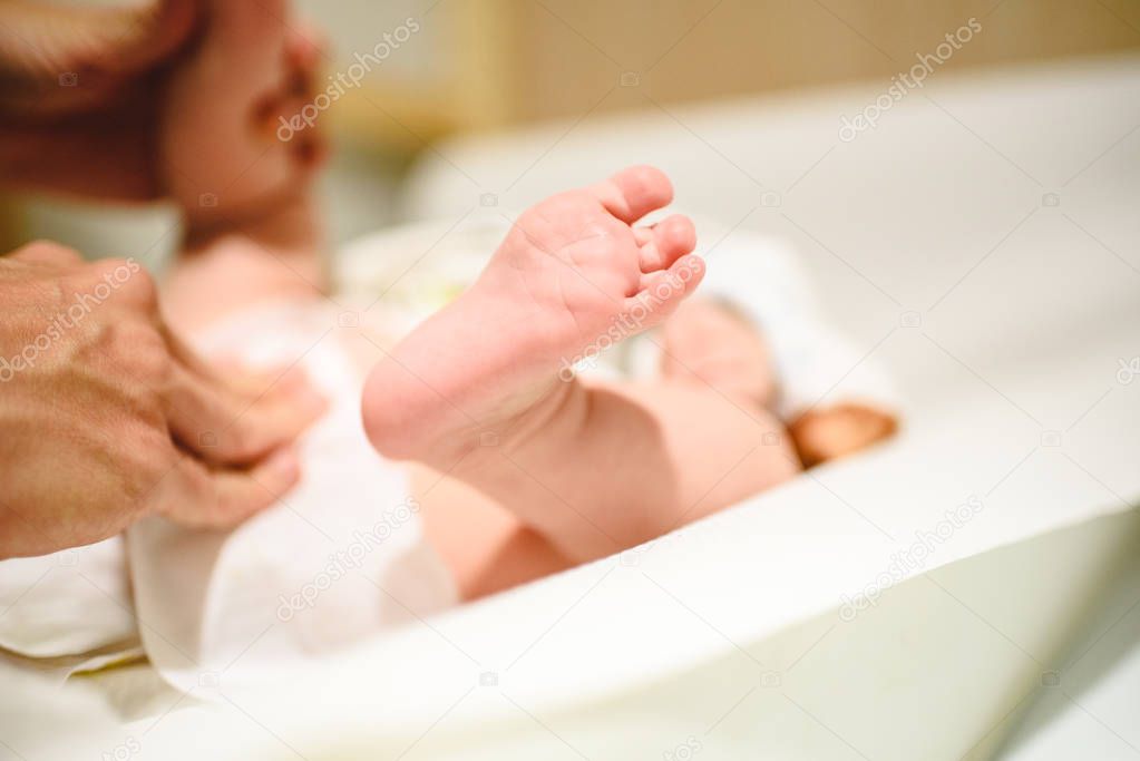 Mother changing diaper to baby, bare foot of her baby.