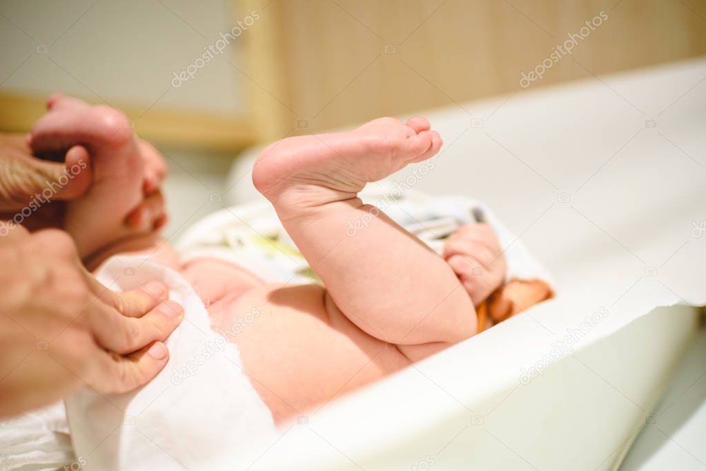 Mother changing diaper to baby, bare foot of her baby.