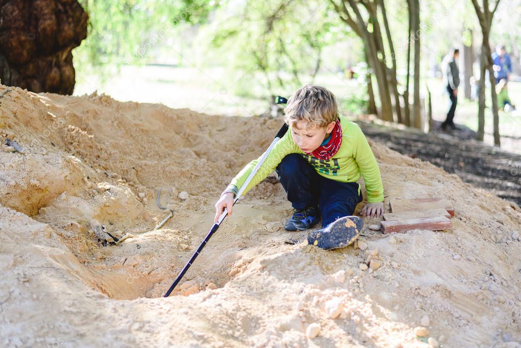 5 year old blond boy playing on a mound of dirt without hygiene digging holes.