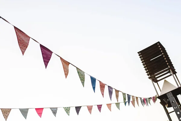 Pennants with blue sky background and pale colors hanging on a rope crossing the image during an outdoor event, space for text.