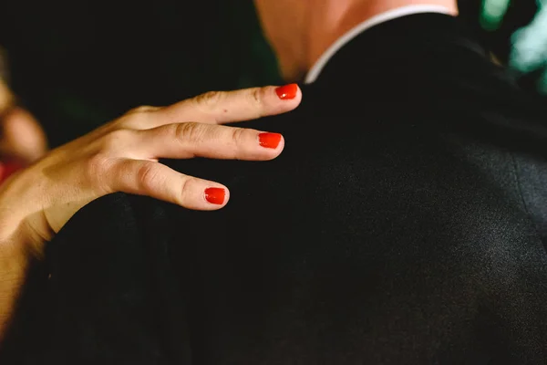 Woman\'s hand with red nails on shoulder of her boyfriend in love.