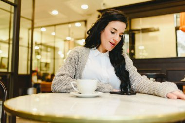 Güzel esmer kadın kahve içme retro bir restoranda kahvaltı yaparken onun smartphone kontrol.