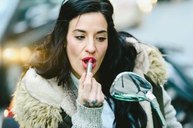 Güzel esmer kadın, orta yaş, kırmızı dudakları bir aynada bir motosiklet boyama.