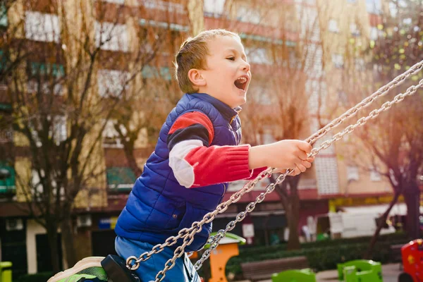 Niño feliz balanceándose en un parque de la ciudad con una gran sonrisa —  Fotos de Stock