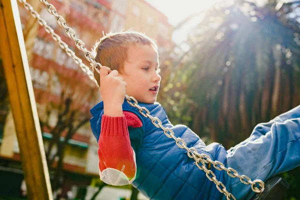 Niño feliz balanceándose en un parque de la ciudad con una gran sonrisa —  Fotos de Stock