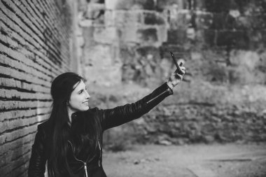 Bin yıllık güzel kadın selfie Fotoğraf blog ya da sosyal ağ posta için bir tuğla duvara yaslanmış iken cep telefonu kullanarak yapma.