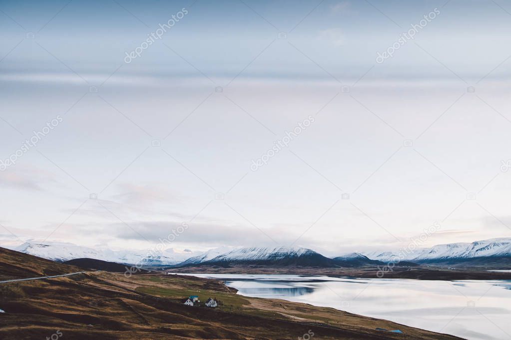 Village with farms in a rural area of the mountains of Iceland, with snowy mountains in the background.