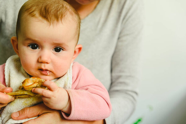 4 month old baby nibbling a chicken leg, tasting his first foods using the method of Baby led weaning BLW.