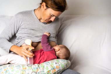 Busy mother breastfeeding her newborn baby while using an manual clipart