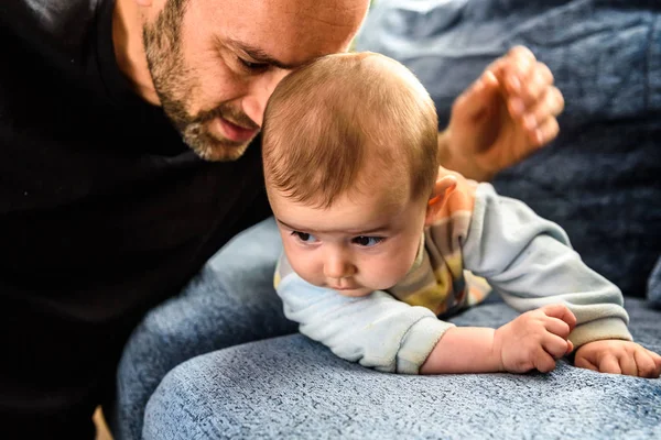 Bebé boca abajo en un sofá explorando su mundo sostenido por su padre — Foto de Stock