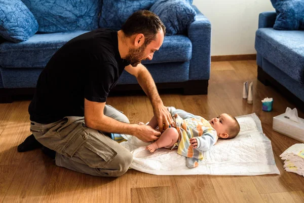 Father changing his daughter\'s dirty diaper on the living room f