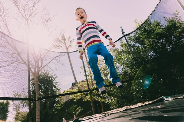 5-летний мальчик прыгает на батуте наслаждаясь своей энергией, лицом — стоковое фото