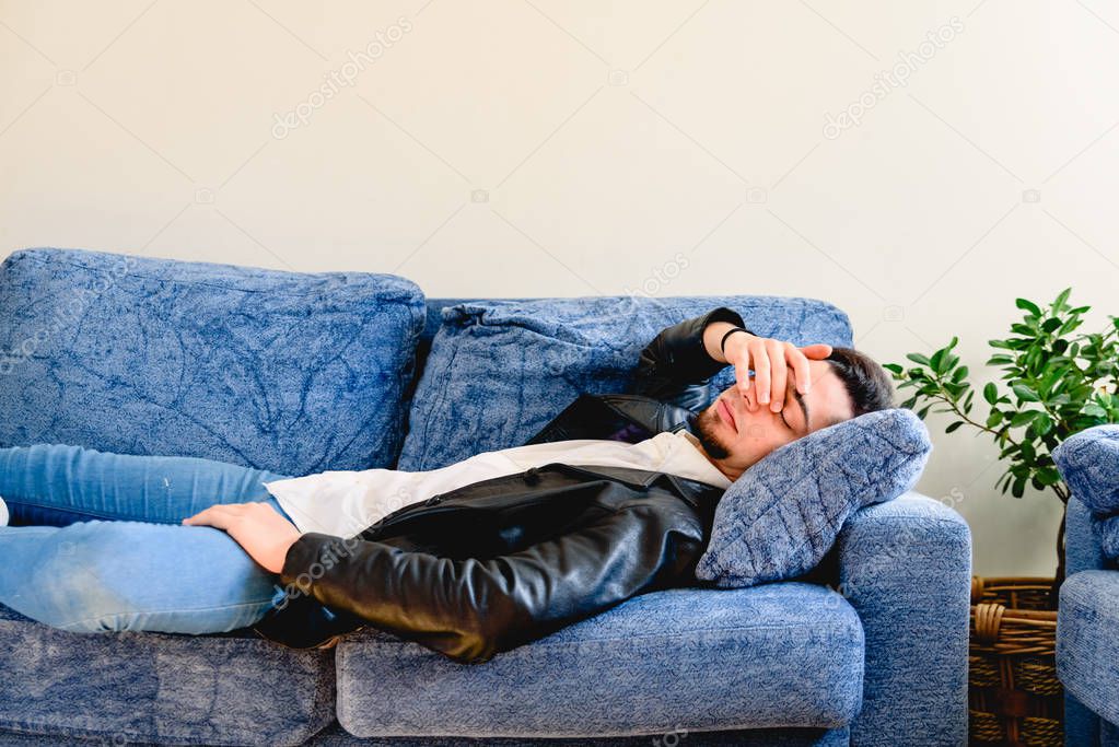 Upset young man lying on couch resting at home feeling fatigue, 