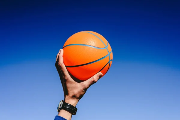 Kezében egy narancsszínű kosárlabda labda a kék ég háttér, én — Stock Fotó
