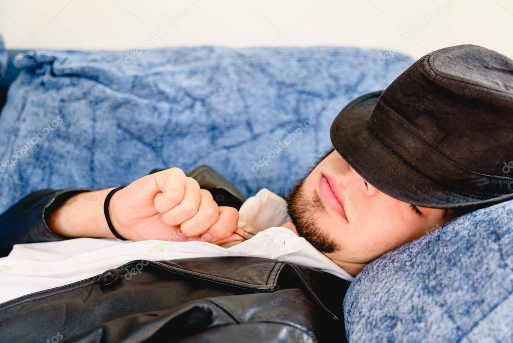 Young man taking a nap with a black hat on the couch at home.