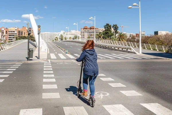 Kvinna på elektrisk skoter korsar en gata utan bilar på en bi — Stockfoto