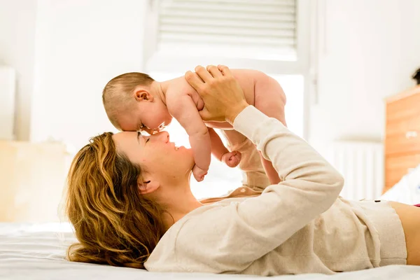 Baby lifted in arms by his mother lying on the bed while playing — Stock Photo, Image