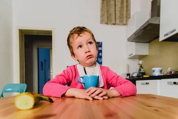 Niño desayunando con expresiones divertidas en una mesa de madera . — Foto de Stock
