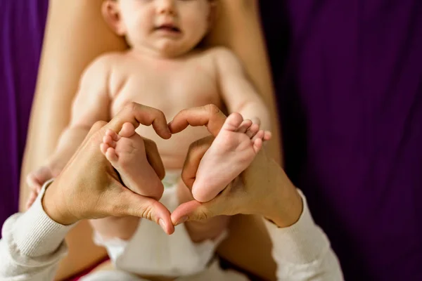 Mom making a heart shape with the feet of her newborn baby. — Stock Photo, Image