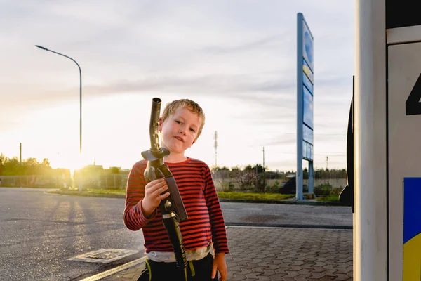 儿童在日落时在加油站握住燃油泵的软管 — 图库照片