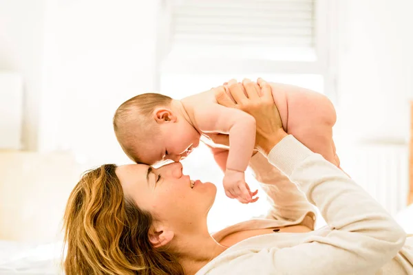 Mom taking care and pampering her newborn baby in the bedroom in — Stock Photo, Image