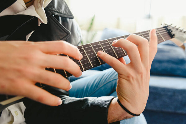 Young man practicing with his electric guitar on the sofa of his