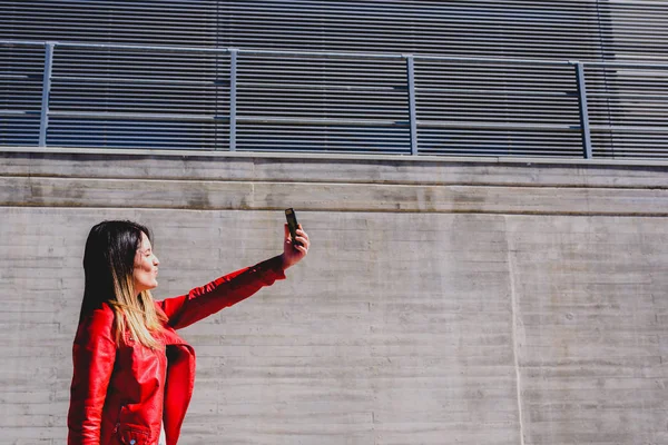 Mujer joven fotografiándose con su teléfono para enviar un selfi — Foto de Stock