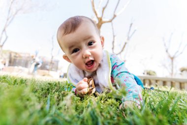 Bebek çimenlerin üzerinde yüzüstü yatarak başını kaldırıyor..
