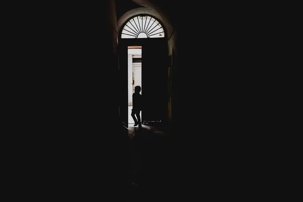 Bambino che esce attraverso una porta retroilluminata, concetto di solitudine e — Foto Stock