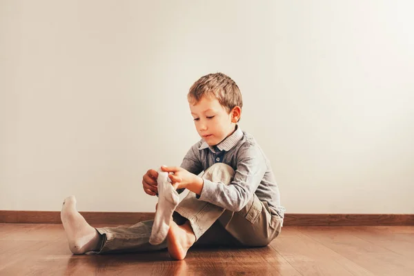 Child sitting on the floor putting on his socks with an expressi — Stock Photo, Image