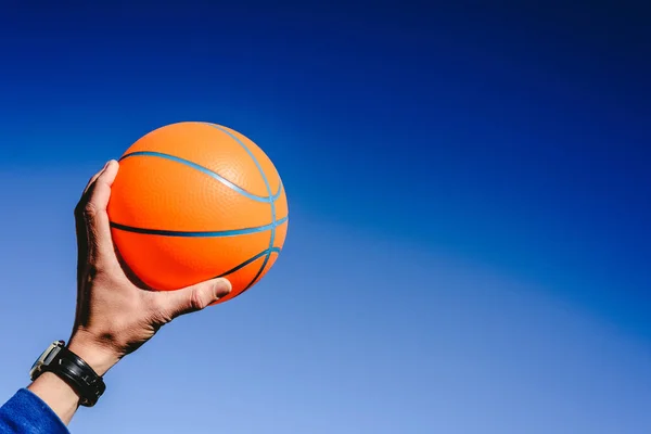 Kezében egy narancsszínű kosárlabda labda a kék ég háttér, én — Stock Fotó