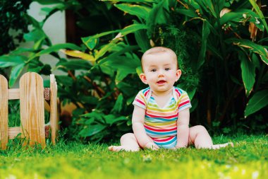 Bebek sevimli bir gülümseme ile yalınayak çim üzerinde oturan.