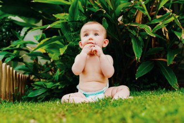 Bebek bezi içinde giysi olmadan çim üzerinde oturan bir f kemirme