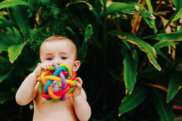 Baby sitting on the barefoot grass nibbling on a plastic toy. — Stock Photo, Image