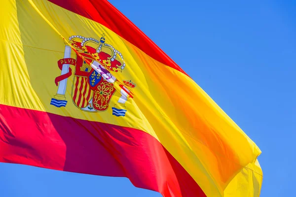 Bandera de España roja y amarilla con escudo real ondeando en el viento i — Foto de Stock