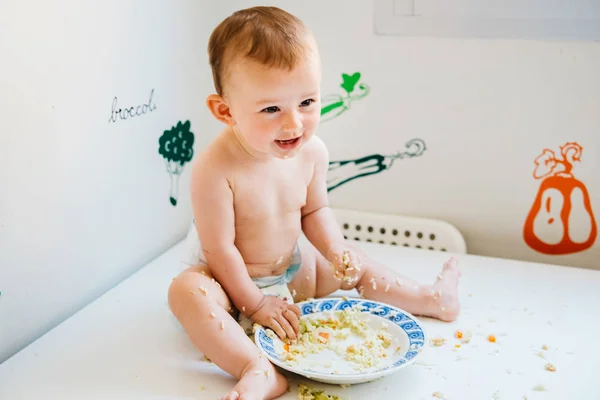 Bebé sonriendo mientras prueba su primer alimento sólido por sí mismo, alte — Foto de Stock