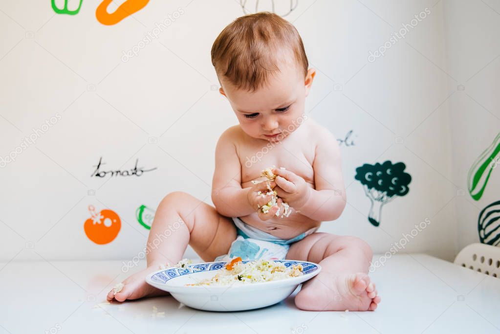 Baby taking handfuls of food to put in his mouth and eat them.