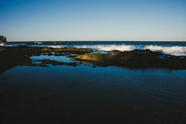 Piccole onde di un mare calmo raggiungono la riva con rocce al crepuscolo , — Foto Stock