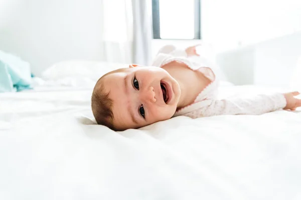 Happy and smiling adorable 6 month old baby girl lying on a bed, — Stock Photo, Image