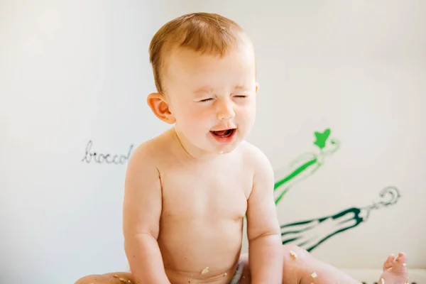 Baby smiling while testing his first solid food by himself, alte