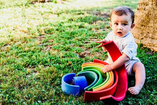 Bebé jugando con un colorido arco iris de madera en la hierba, childr —  Fotos de Stock