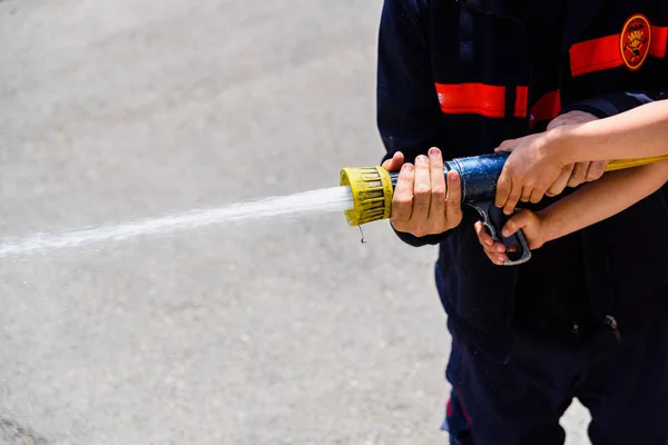 Firefighter demonstrating how to use a water hose to children du — Stock Photo, Image