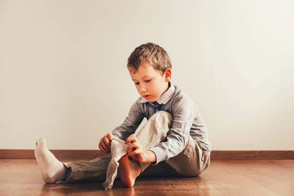 Child sitting on the floor putting on his socks with an expressi
