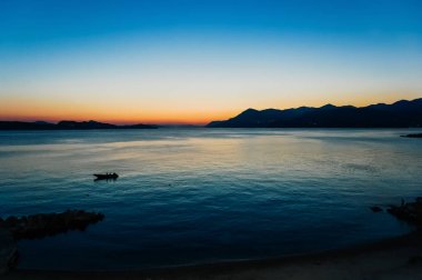 Arka planda dağlar ve küçük bir boa ile bir koyda gün batımı