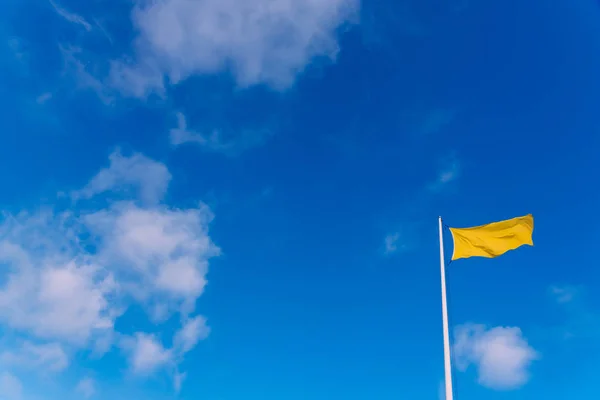 Bandeira de tecido amarelo acenando ao vento com o fundo de um c — Fotografia de Stock