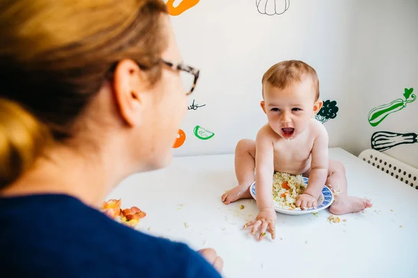 Bebé sonriendo felizmente a su madre mirándolo mientras come w — Foto de Stock
