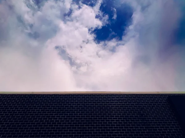 Achtergrond van een muur met donker blauwe baksteen en hemel met wolken. — Stockfoto