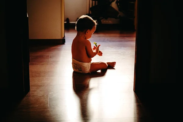 Barnet sitter på ryggen på ett trägolv i sitt hus ser — Stockfoto