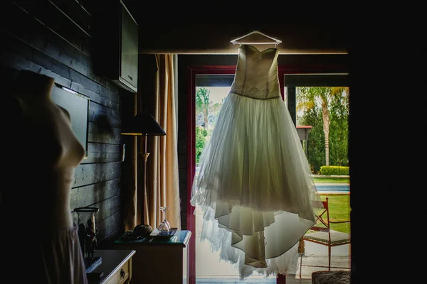 Wedding dress hanging in a hotel room on the day of the wedding.